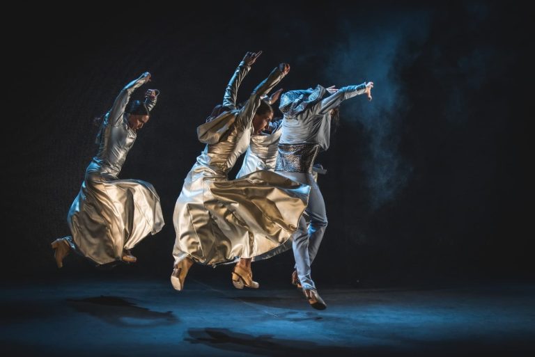 Mujeres bailando flamenco en el escenario fondo oscuro con hombre en el medio