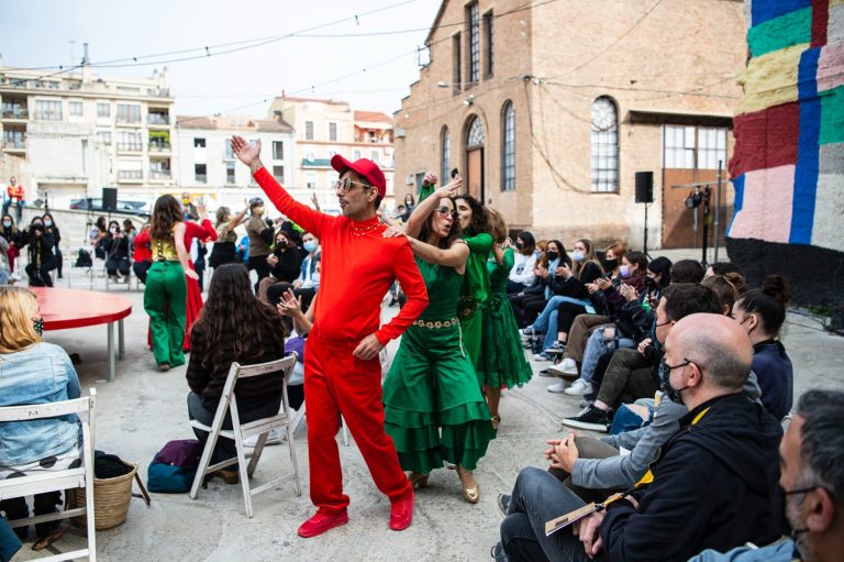 Un hombre vestido de rojo con gorra roja y gafas seguido por mujeres baila en la calle en una apresentación