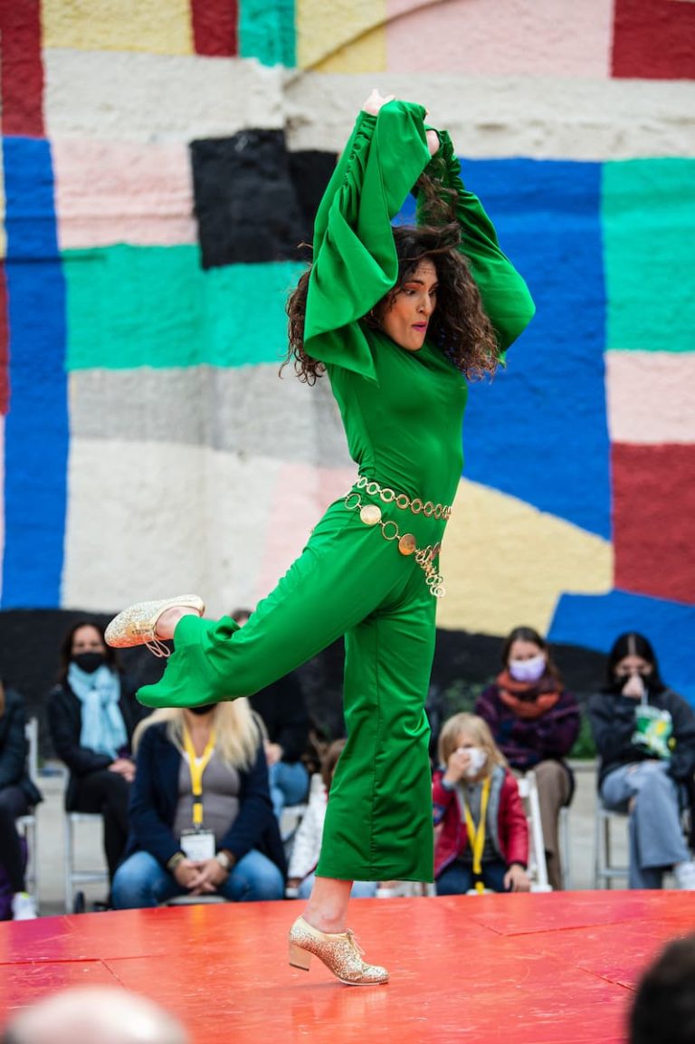 Mujer vestida de verde hace movimiento de baile flamenco en un espectáculo de calle