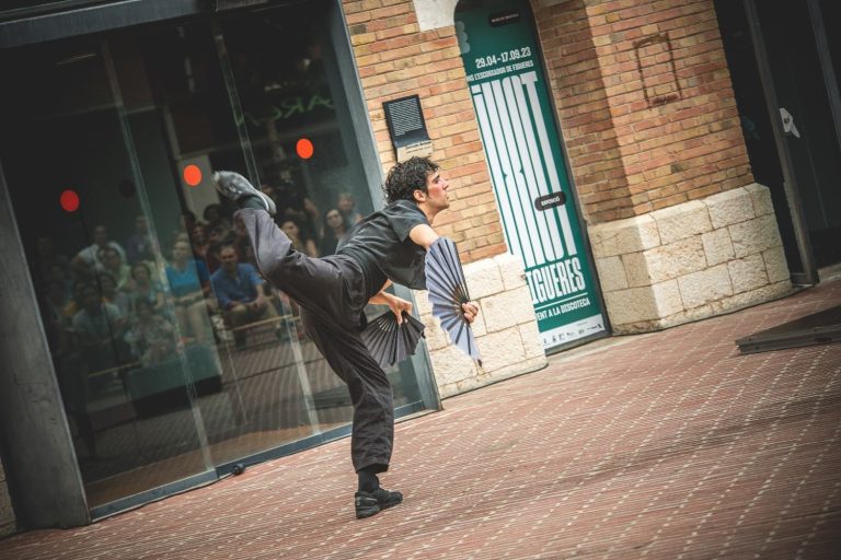 Hombre con ropa negra bailando y haciendo movimientos acrobáticos en un espectáculo de calle