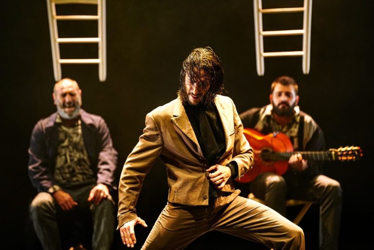 bailaor de flamenco con ropa marrón bailando en un escenario con músicos al fondo